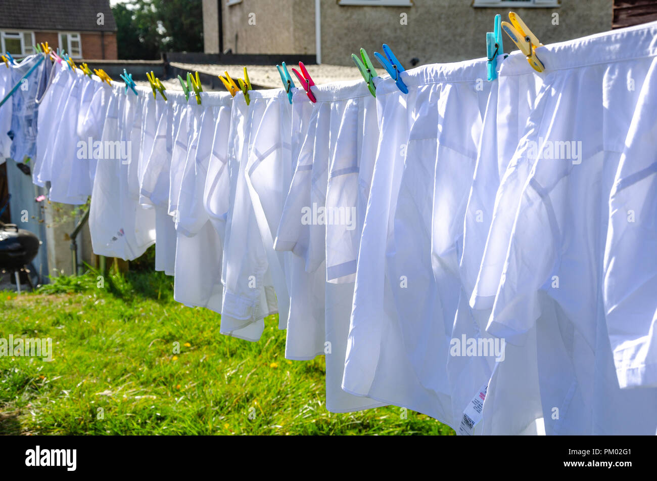 Camicie bianche appendere fuori ad asciugare su una linea di lavaggio in una zona residenziale giardino sul retro. Foto Stock