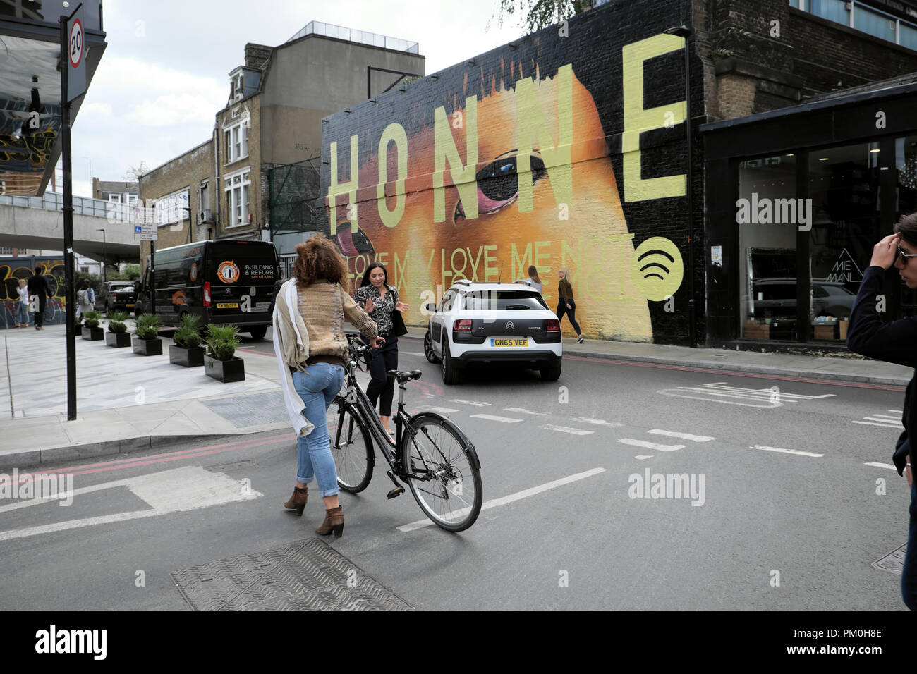 Donna che cammina con la bici in strada dal cittadino M Hotel passato HONNE carta murale street art pittura su Holywell Ln Shoreditch East London REGNO UNITO KATHY DEWITT Foto Stock