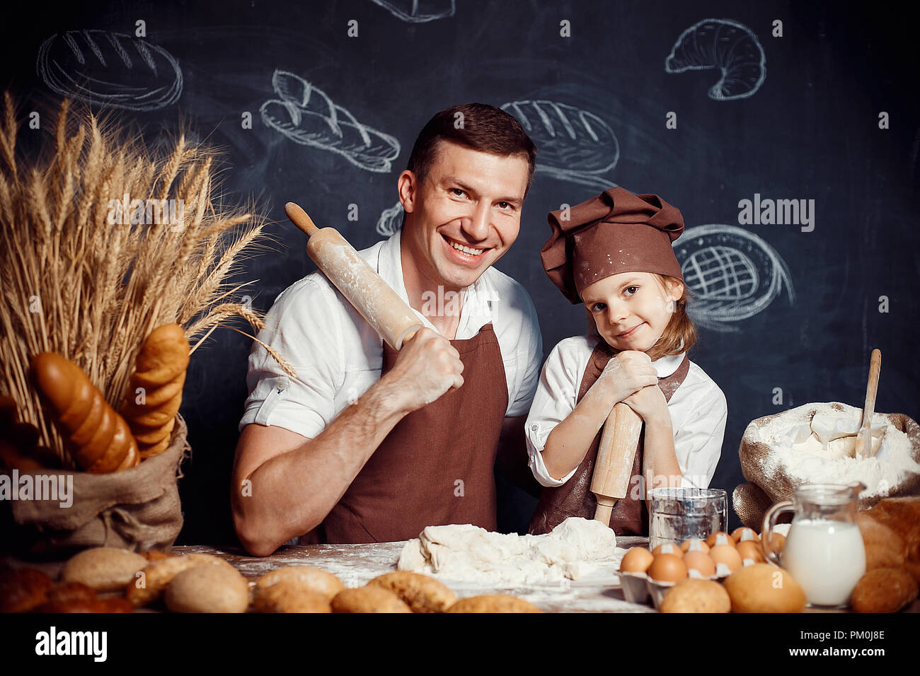 Adulto felice l'uomo con la bambina indossando grembiuli e trattenere i perni di rotolamento guardando la fotocamera mentre si effettua la pasta di pane Foto Stock