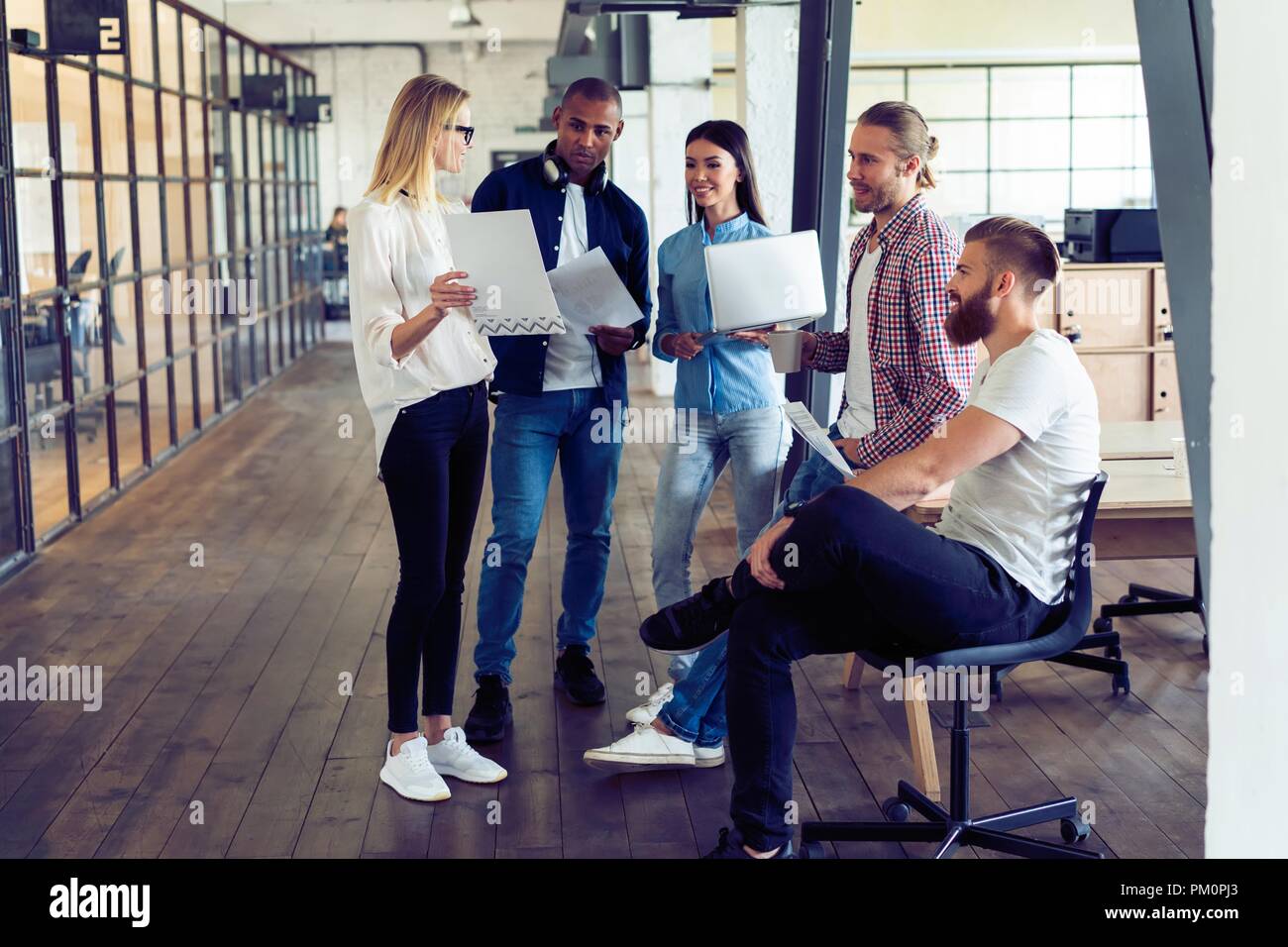 Un lavoro di squadra. Per tutta la lunghezza della giovane gente moderna in smart casual pianificazione della strategia di business mentre la giovane donna puntando al grande carta in ufficio corridoio. Foto Stock