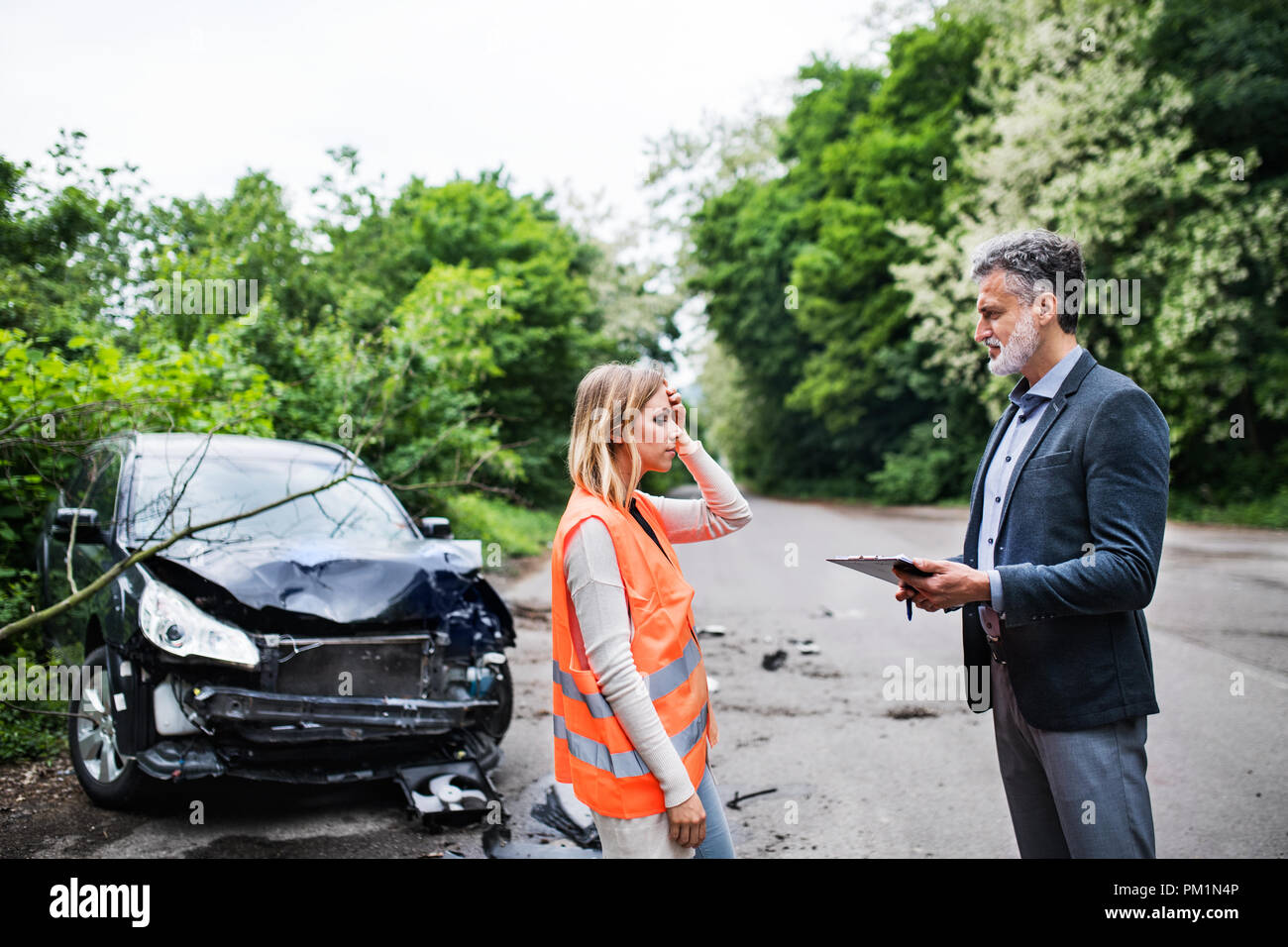 Un agente di assicurazione a parlare con una donna conducente tramite l'auto sulla strada dopo un incidente. Foto Stock