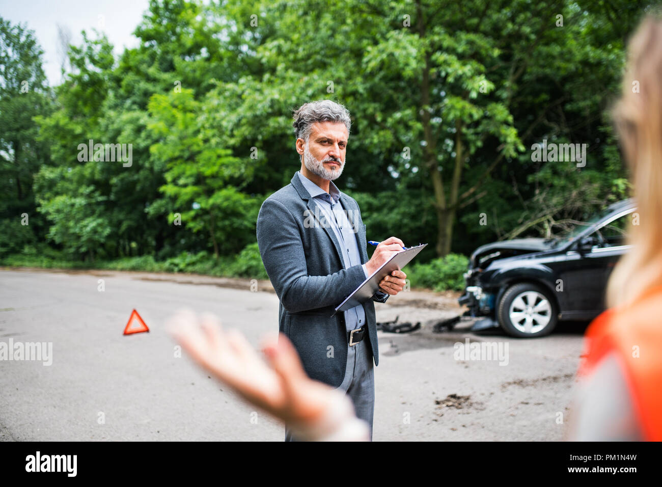Un agente di assicurazione a parlare con una donna al di fuori sulla strada dopo un incidente di automobile. Foto Stock