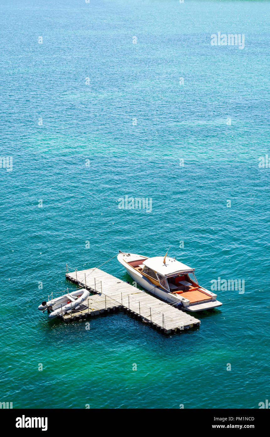 Un lussuoso motoscafo ormeggiato a un isolato, a forma di t, dock in legno in acque verdi con un gommone posa sul dock. Foto Stock