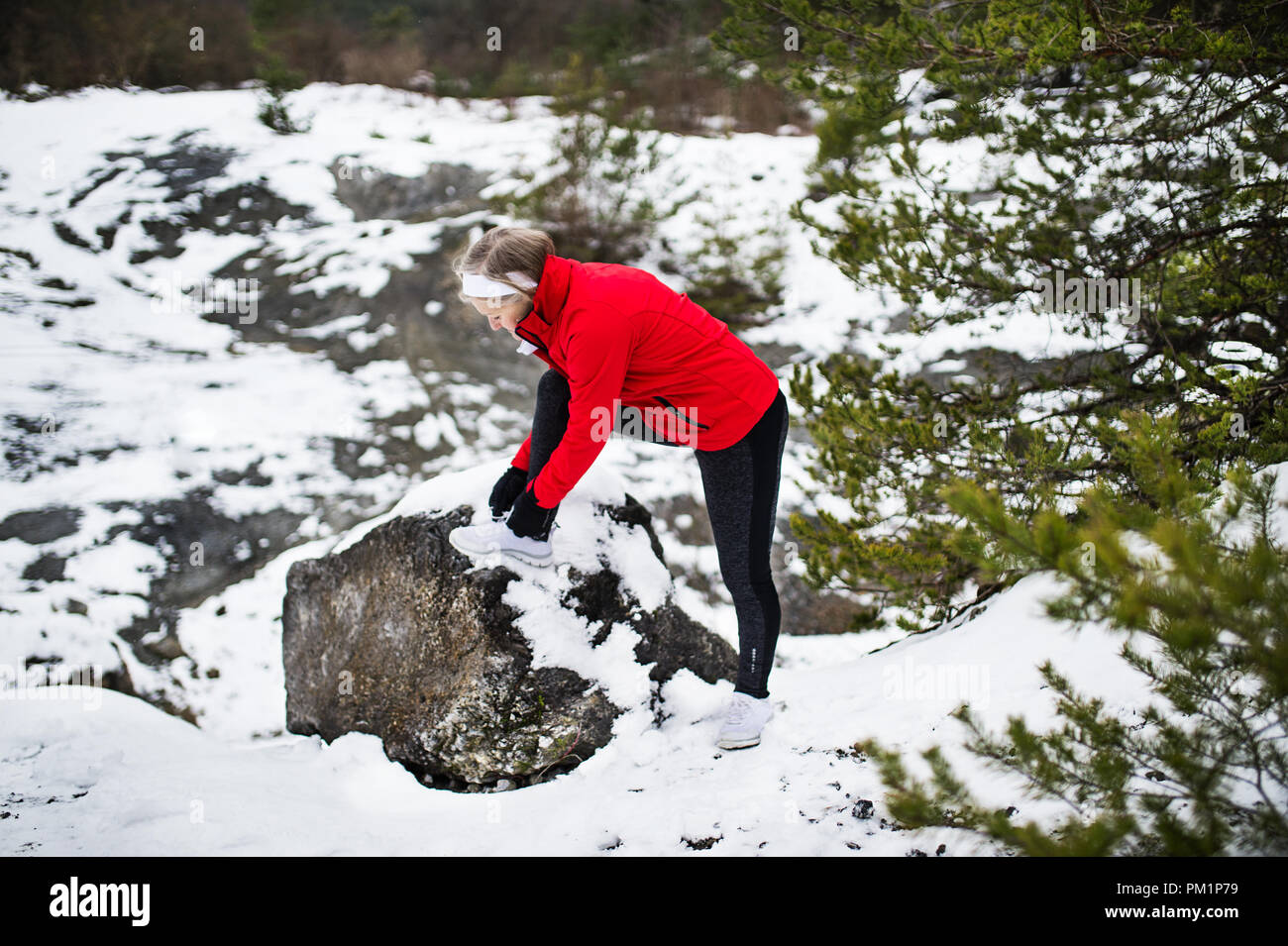Un senior donna runner legatura di lacci delle scarpe in inverno la natura. Foto Stock