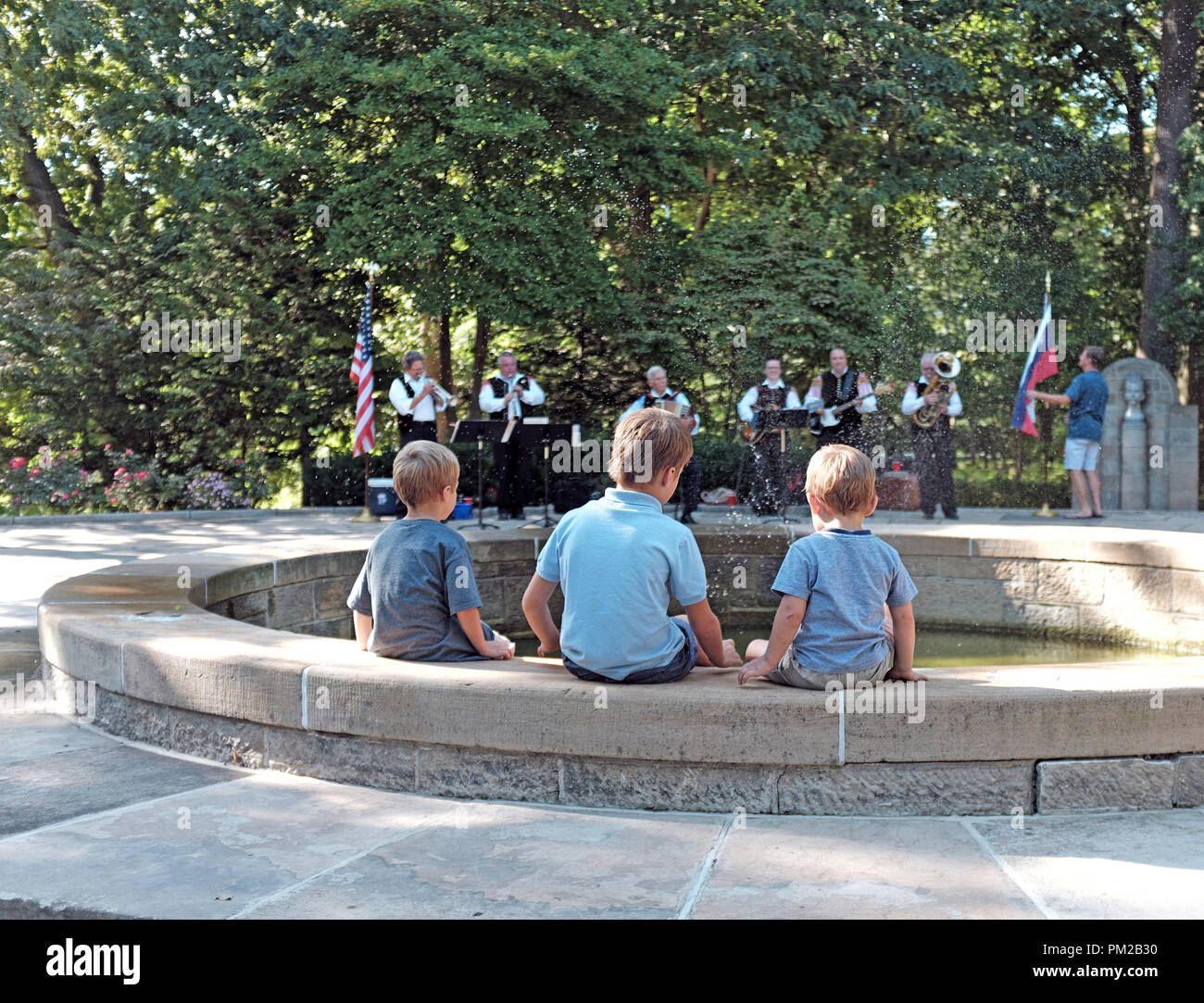 Cleveland, Ohio, USA. 16 Settembre, 2018. Tre ragazzi raffreddarsi lungo il bordo di una fontana di acqua durante la partecipazione alla 73Uno annuale Giornata Mondiale celebrazione in Cleveland, Ohio, USA. La fontana è in culturale sloveno giardino, uno dei trenta completato giardini culturali che rappresentano le comunità di immigrati in Cleveland Ohio area. Sullo sfondo di una band suona musica etnica come parte della giornata di festa che si verifica ogni settembre nei giardini culturale situato nel Parco di Rockefeller. Credito: Mark Kanning/Alamy Live News. Credito: Mark Kanning/Alamy Live News Foto Stock