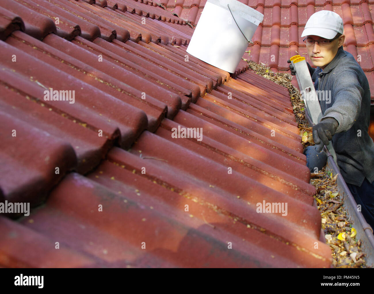 L'uomo sulla scala pulisce le grondaie sul tetto. Primavera e autunno problema con foglie in gronda. Foto Stock