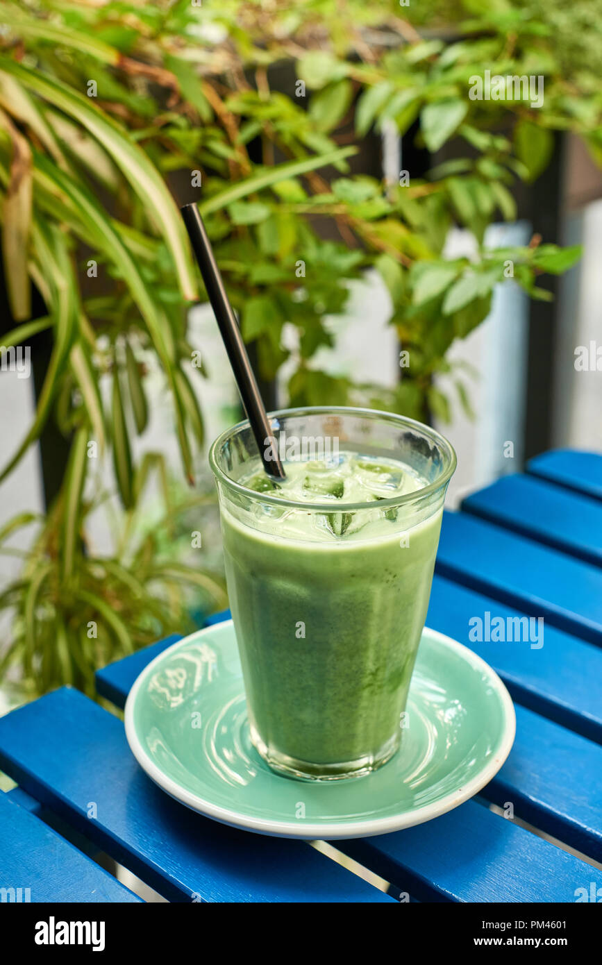 Iced matcha latte nel bicchiere con una cannuccia su sfondo blu (tavolo in legno) Foto Stock