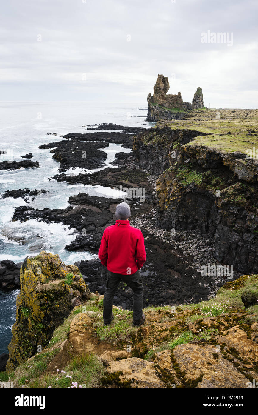 Londrangar scogliere di basalto. Tourist guy stand su una roccia e guarda all'oceano. Famosa attrazione turistica di Islanda Foto Stock