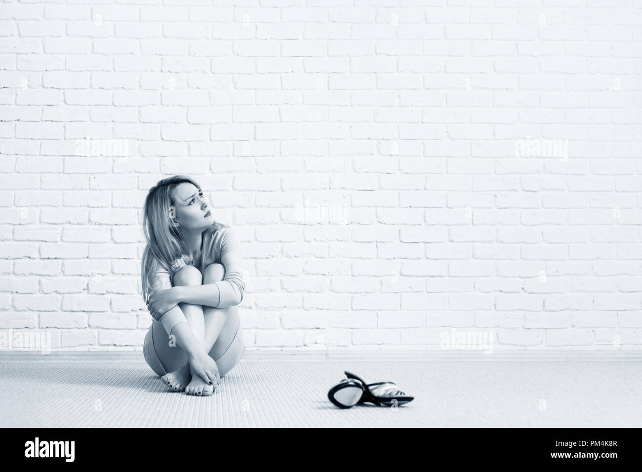 Giovane donna triste nel vestire seduto sul pavimento e guardando lontano. Foto Stock