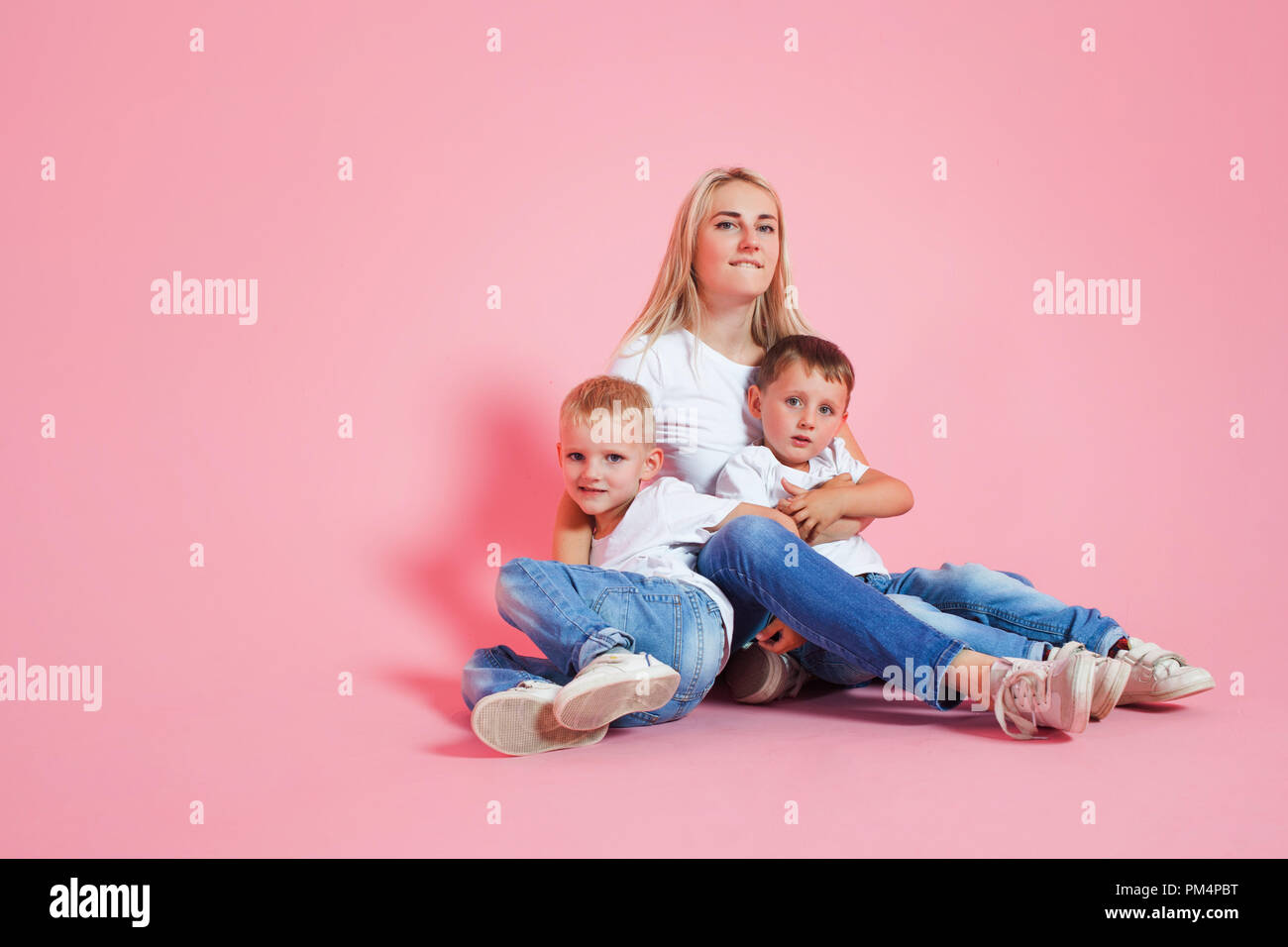 Bella bionda la mamma con due figli felice. Giovane donna e due baby boys, sfondo rosa Foto Stock