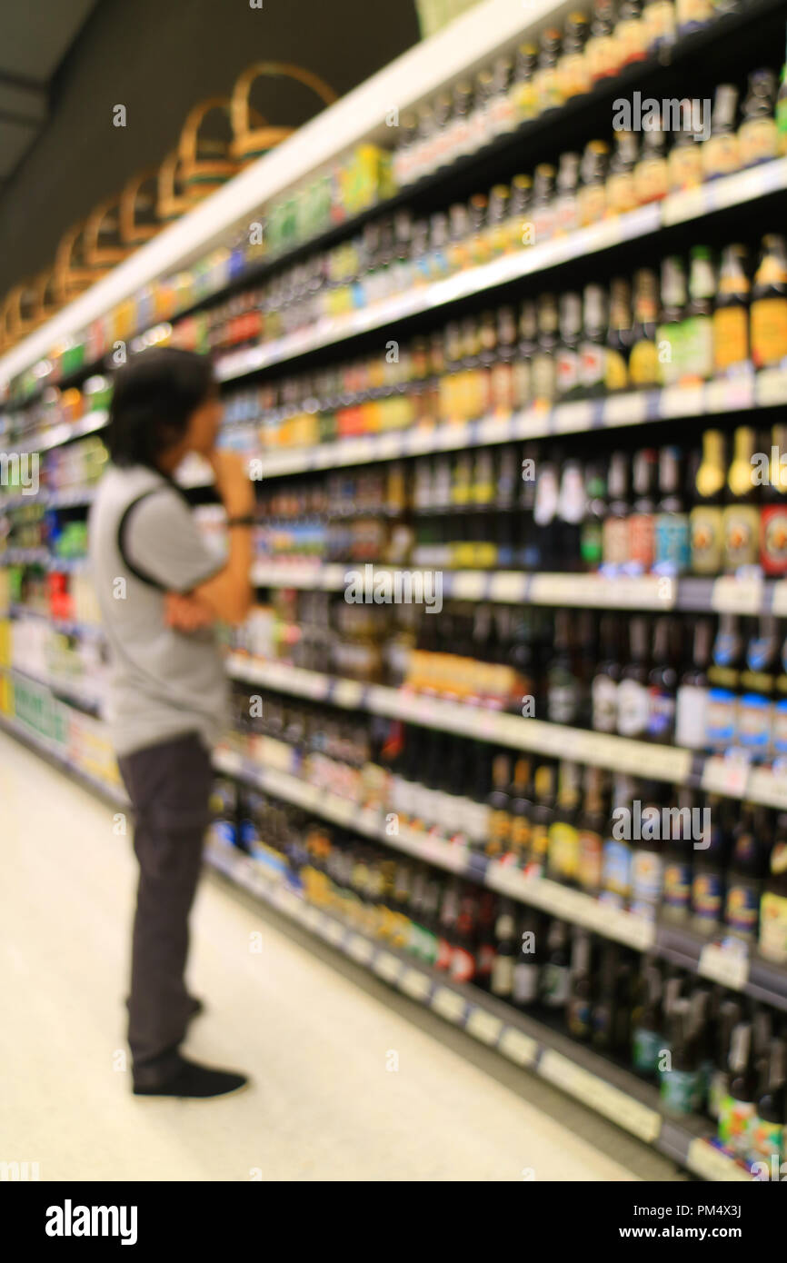 Foto verticale di offuscata giovane scegliendo qualcosa al ripiano di generi alimentari nel negozio al dettaglio Foto Stock