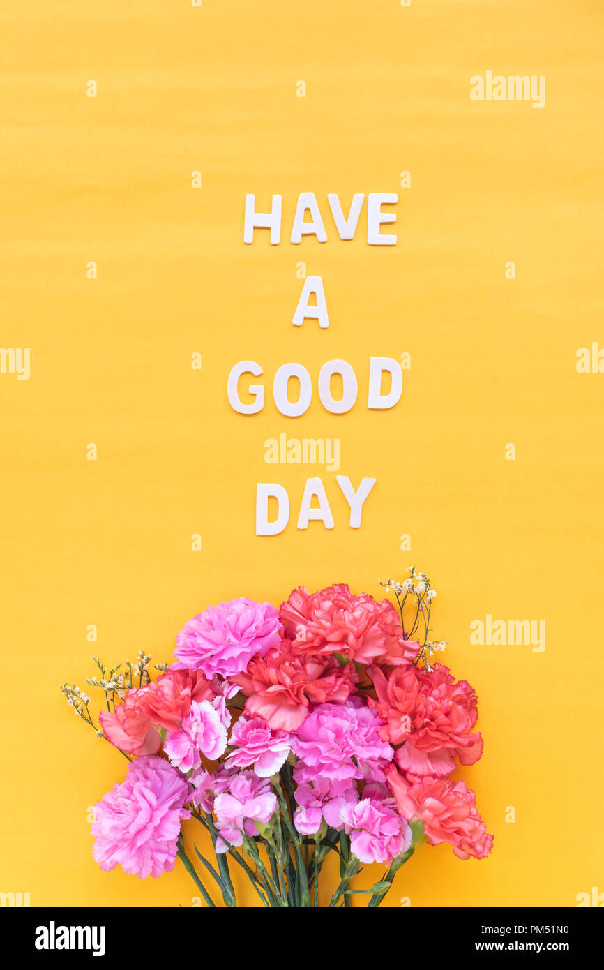 Avere una buona giornata per la parola in legno con fiori freschi garofani luminoso su sfondo giallo Foto Stock