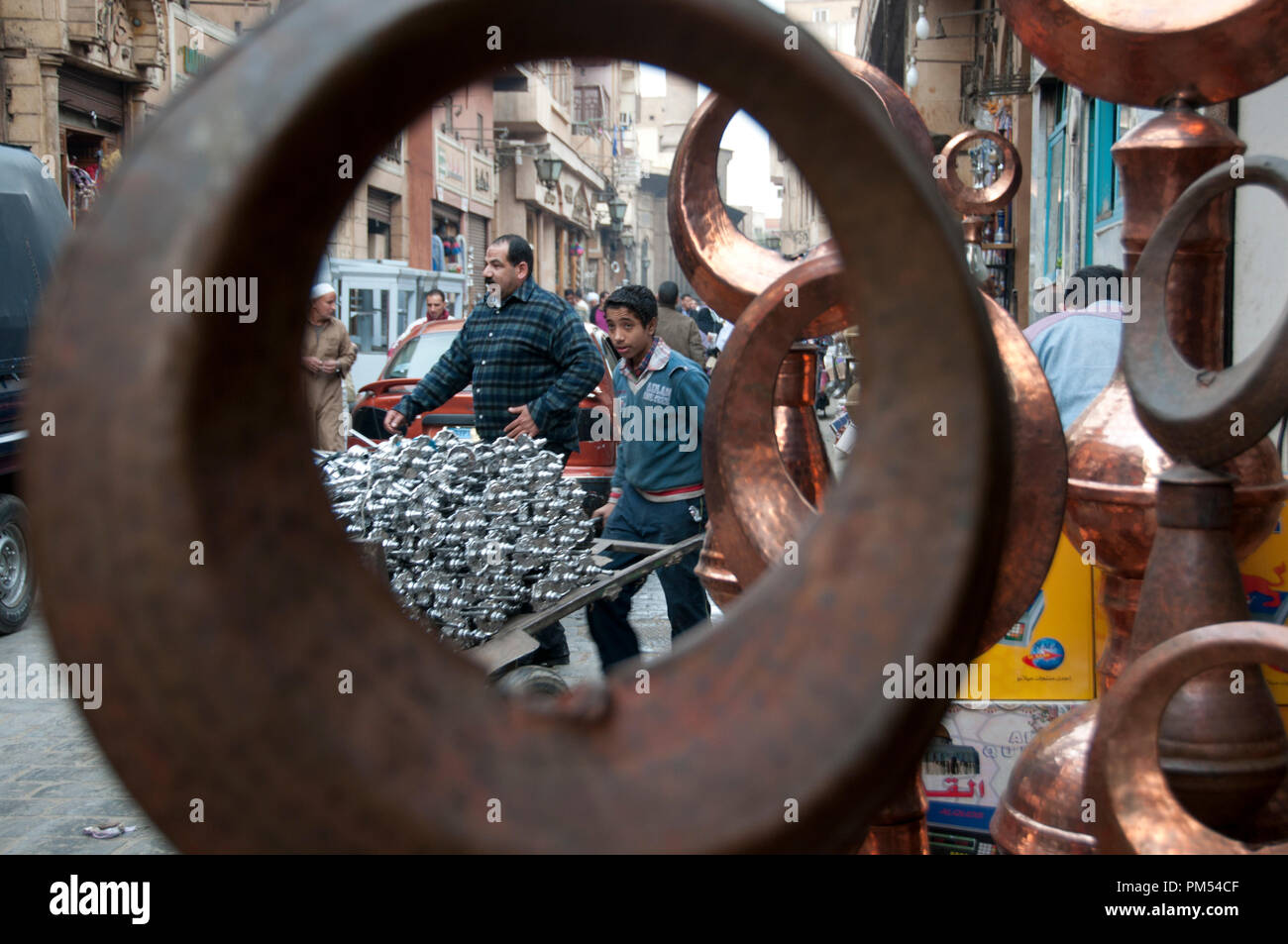 L'Egitto, Il Cairo 2014. Khan al-Khalilli , vecchia area islamica. Ragazzo spingendo un carrello pieno di pipe shisha visto attraverso battuto copperwork. Foto Stock