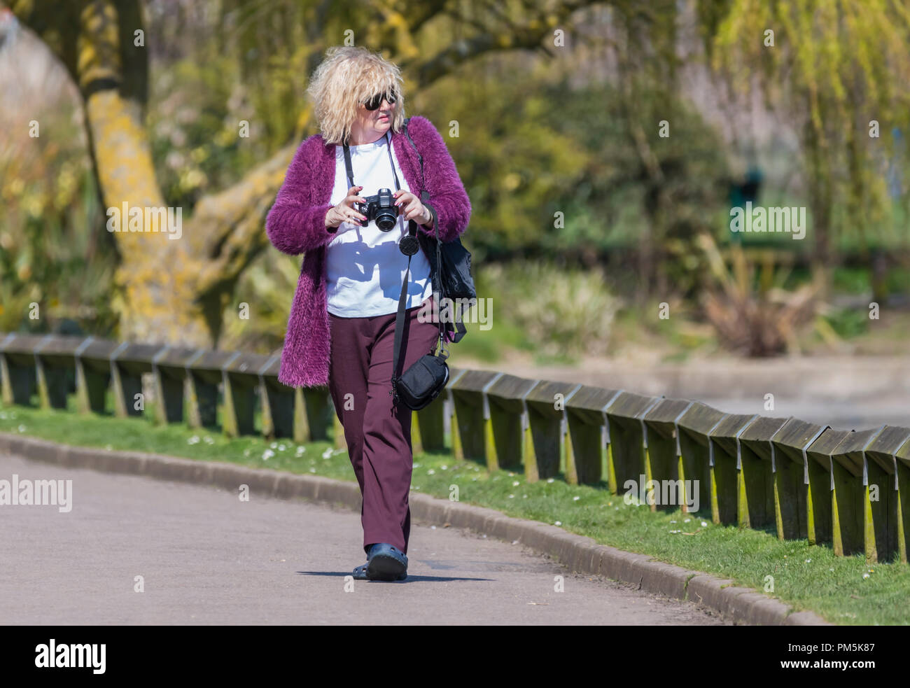 Donna di mezza età a piedi attraverso un parco con una telecamera alla ricerca di cose da fotografare. Foto Stock