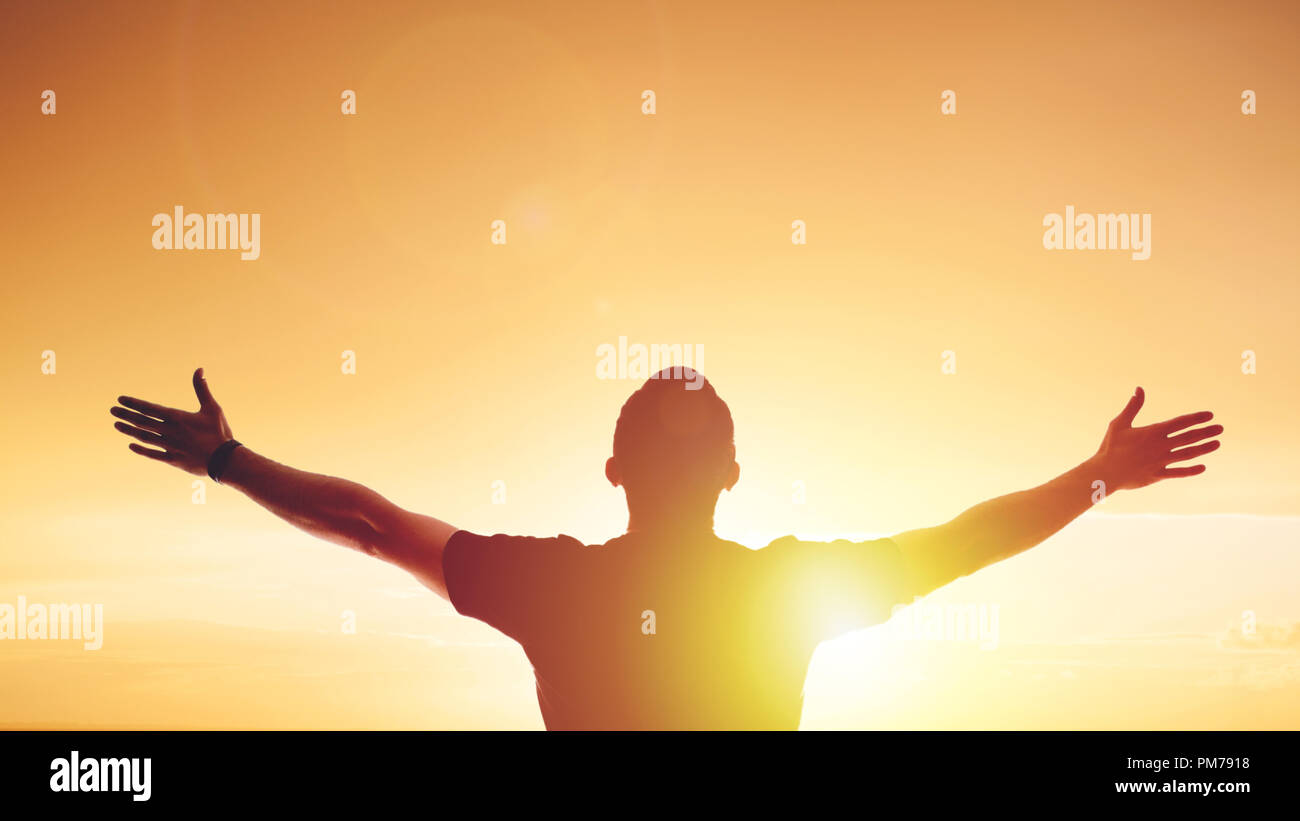 Giovane uomo in piedi tese al tramonto. Luminoso bagliore solare e cielo Foto Stock