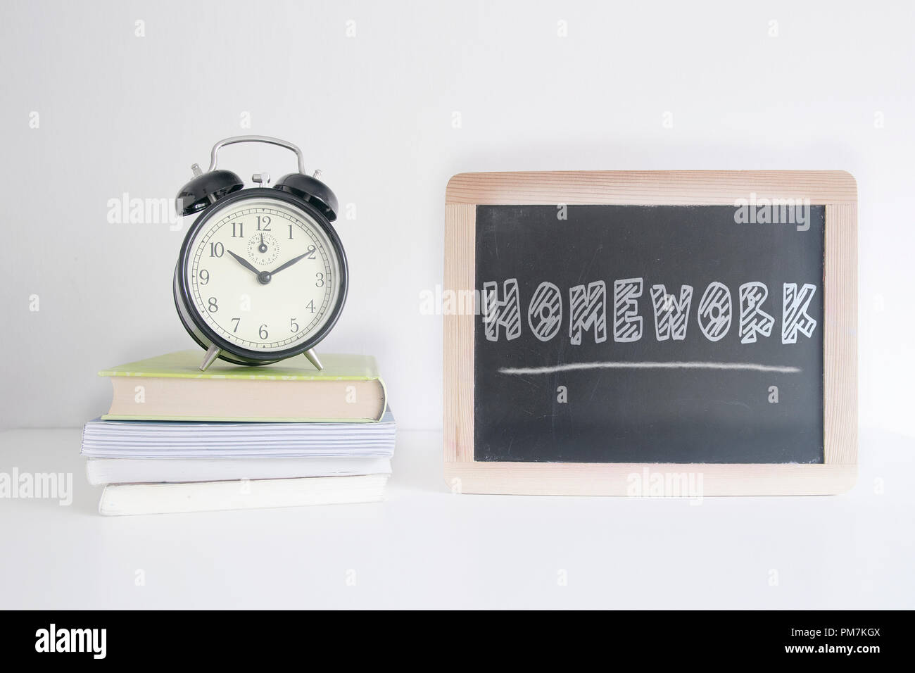 Sveglia su una pila di libri accanto a una lavagna con i compiti di testo scritto su di esso. Svuotare lo spazio di copia per l'editor di testo. Foto Stock
