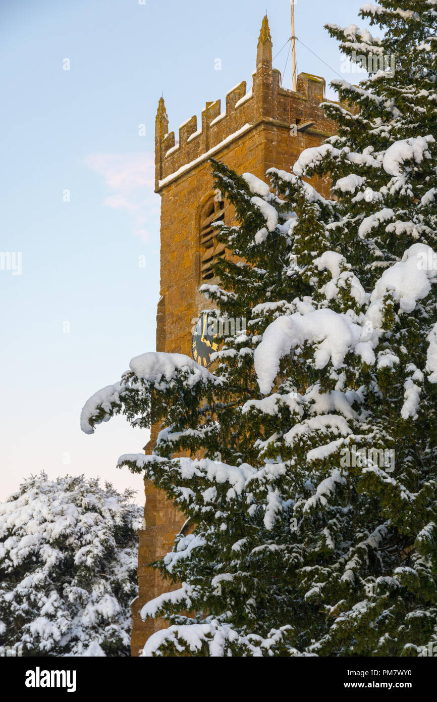 Pietra villaggio inglese chiesa raffigurato nella neve in inverno con cielo chiaro. Foto Stock