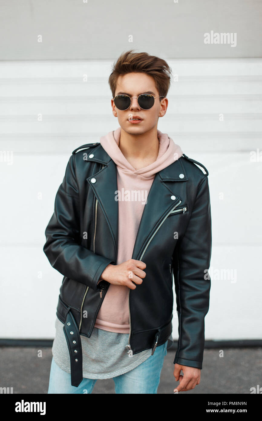 Giovane uomo bello in un marchio nero giacca di pelle e una felpa rosa  vicino a un bianco parete in metallo Foto stock - Alamy