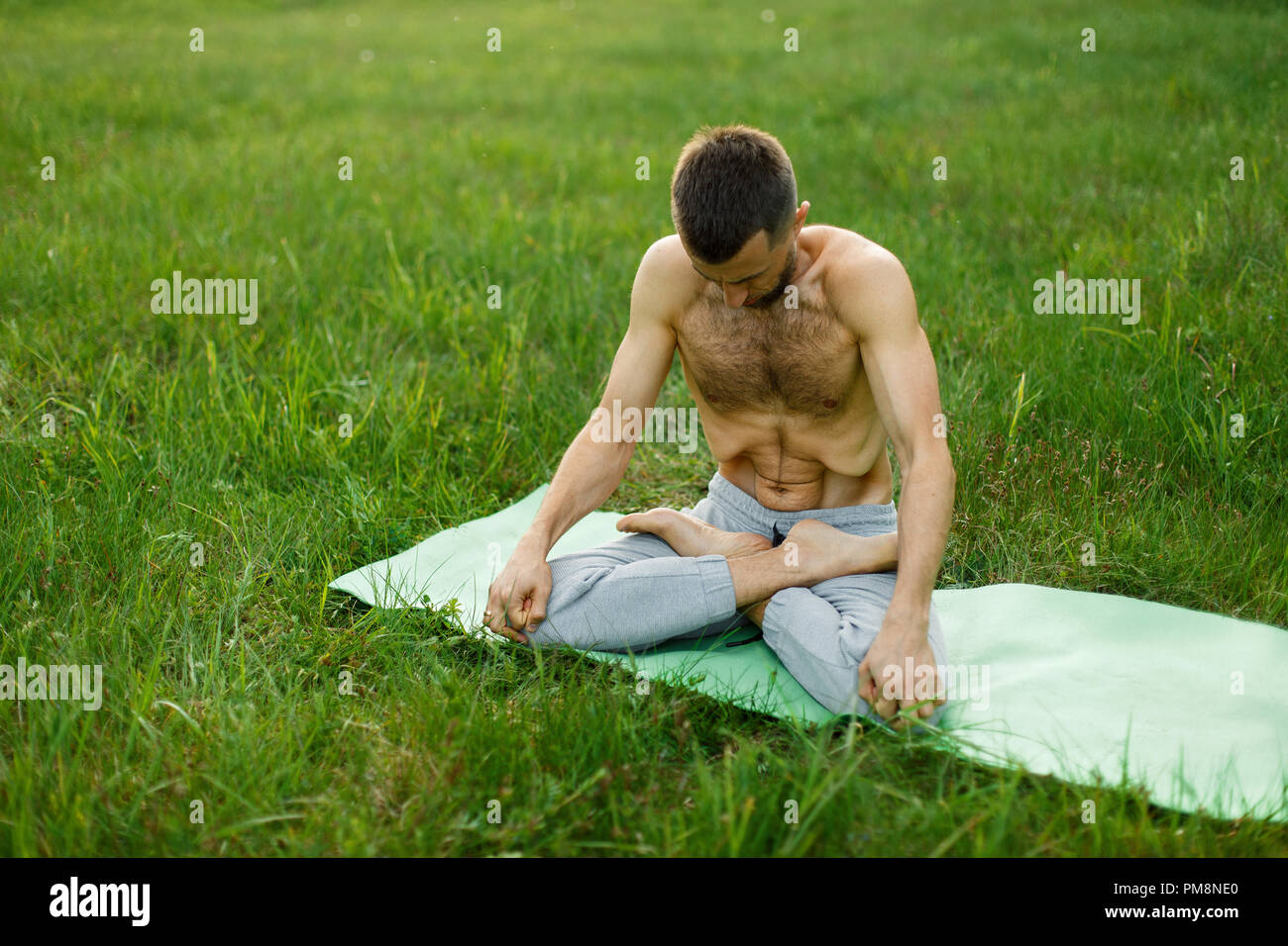 Giovane uomo a praticare yoga su erba verde nel parco. La meditazione. Muscoli addominali Foto Stock
