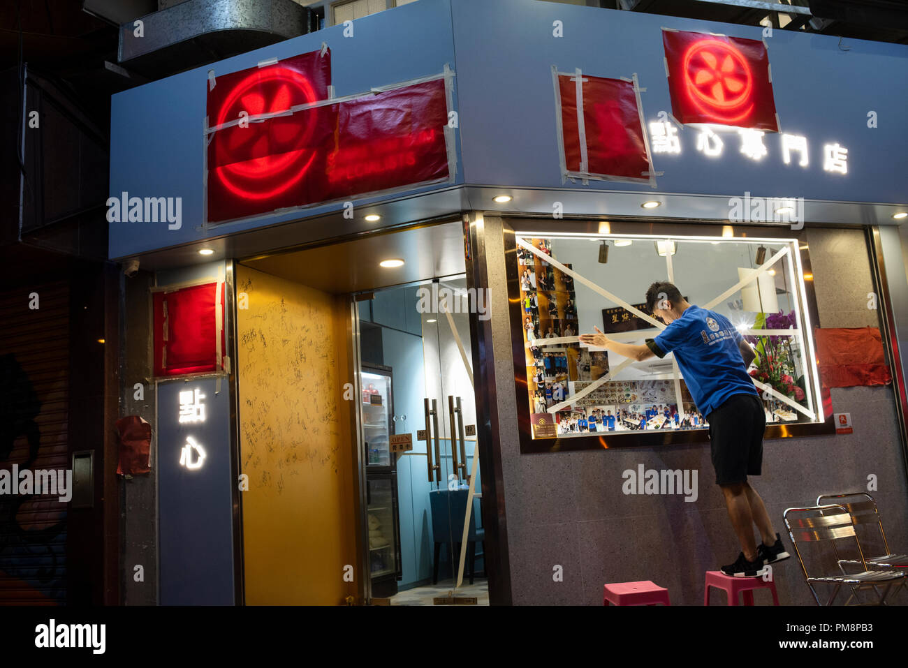 Un ristorante lavoratore nastri fino alla finestra per proteggerlo contro la prossima super typhoon Mangkhut in Hong Kong. È previsto che la terra di domenica con un tifone segnale n. 8. Foto Stock