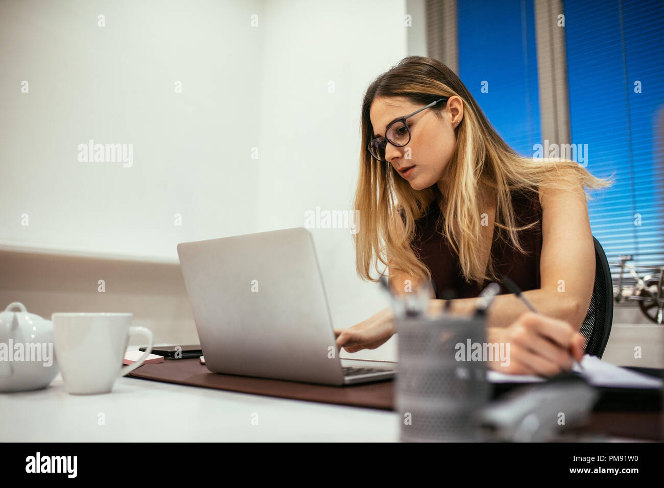 donna d'affari che lavora al computer portatile e prende appunti. Imprenditrice donna seduta in ufficio che lavora. Foto Stock