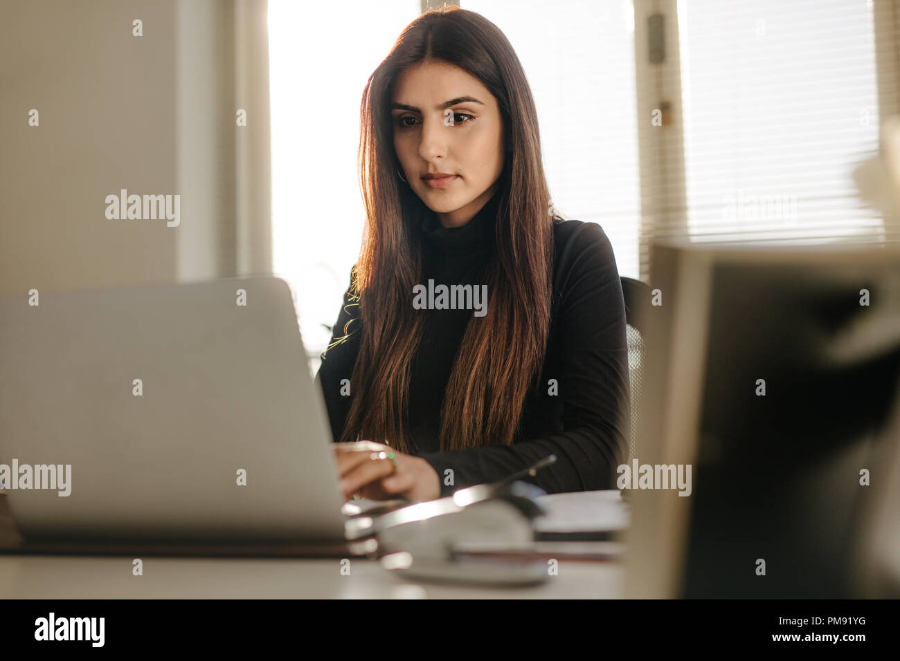 Ritratto di giovane e bella donna seduta alla sua scrivania in ufficio e di lavoro sul computer portatile. Smart giovane femmina in casuals lavorando sul computer portatile in ufficio Foto Stock
