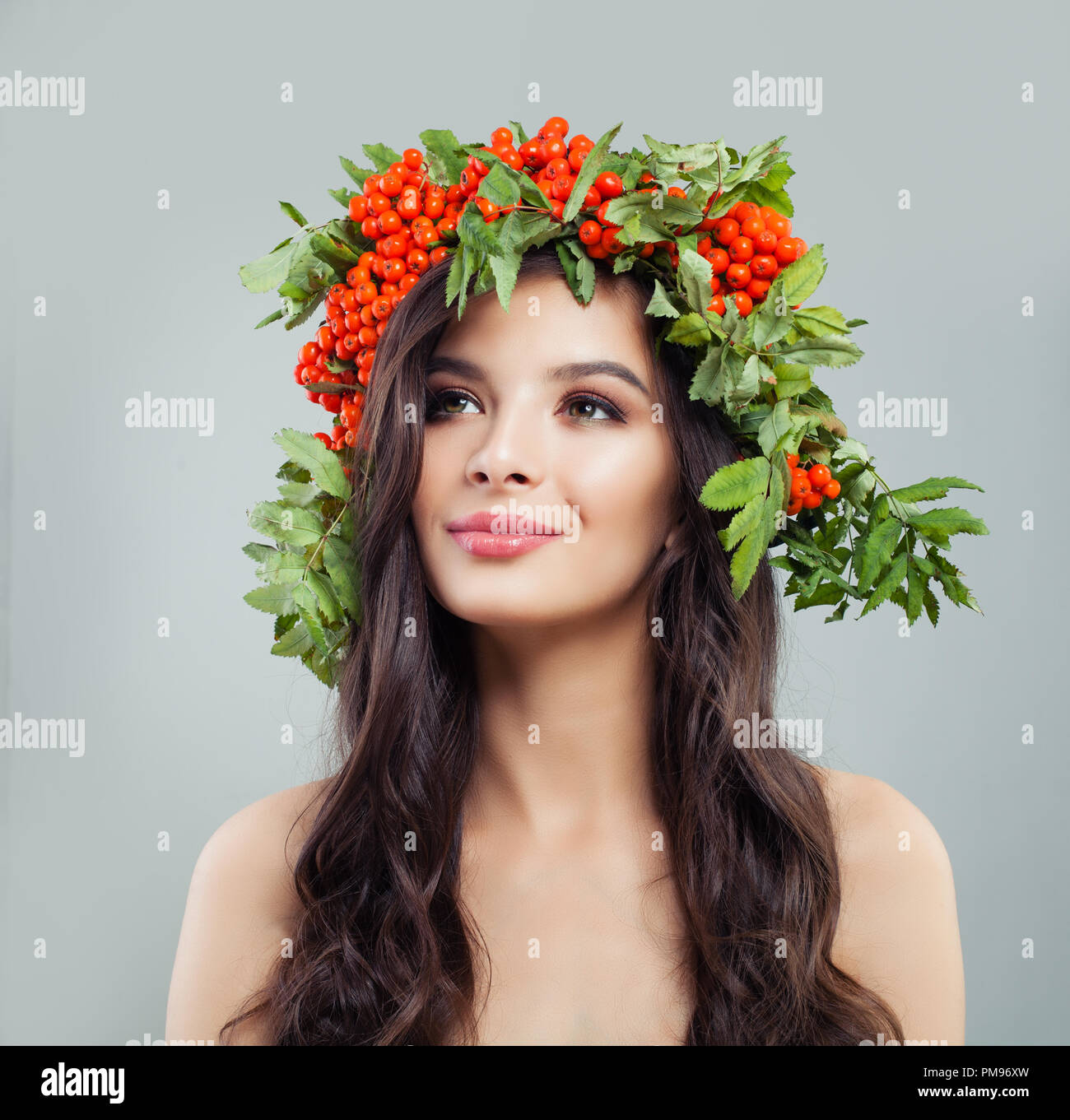 Perfetto giovane donna che guarda verso l'alto. Bruna modello femminile con trucco naturale, lunghi capelli ondulati e rosse bacche e foglie corona Foto Stock