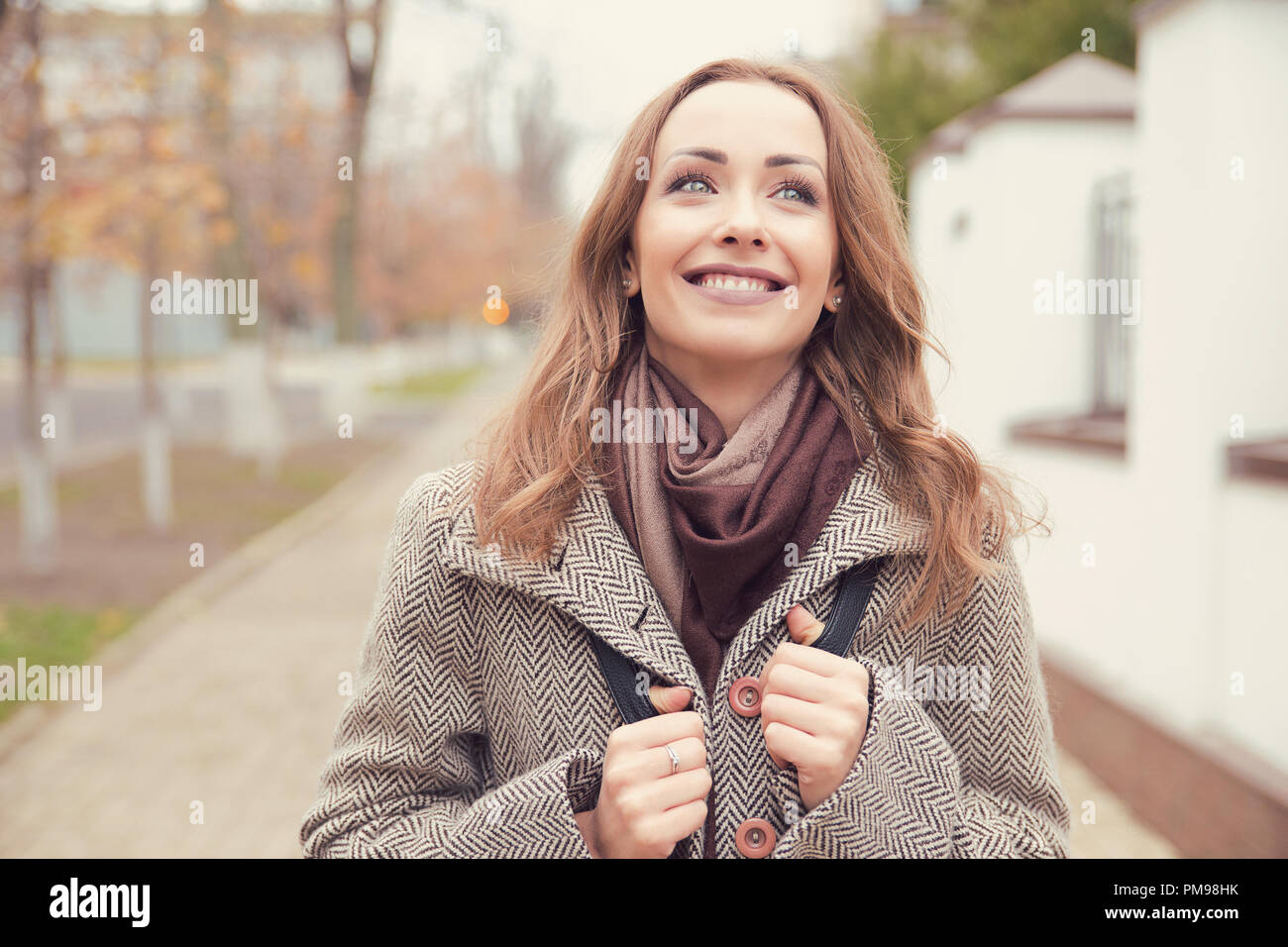 Affascinante giovane donna a camminare su una strada e fantasticando su una giornata autunnale sorridente lontano Foto Stock