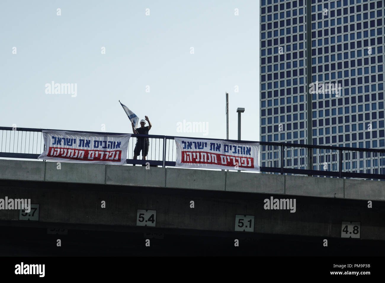 Tel Aviv, Israele. Il 17 settembre 2018. Un uomo solitario onde una bandiera israeliana sulla pace HaShalom ponte sopra il Tel Aviv Ayalon Freeway con banner ebraico la lettura di "noi amiamo Israele, parte da Netanyahu". Credito: Nir Alon/Alamy Live News Foto Stock