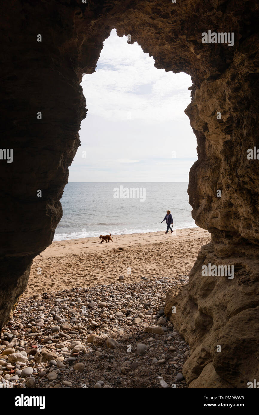 Donna cane a piedi lungo la spiaggia incorniciata da una grotta, Seaham, Co. Durham, England, Regno Unito Foto Stock