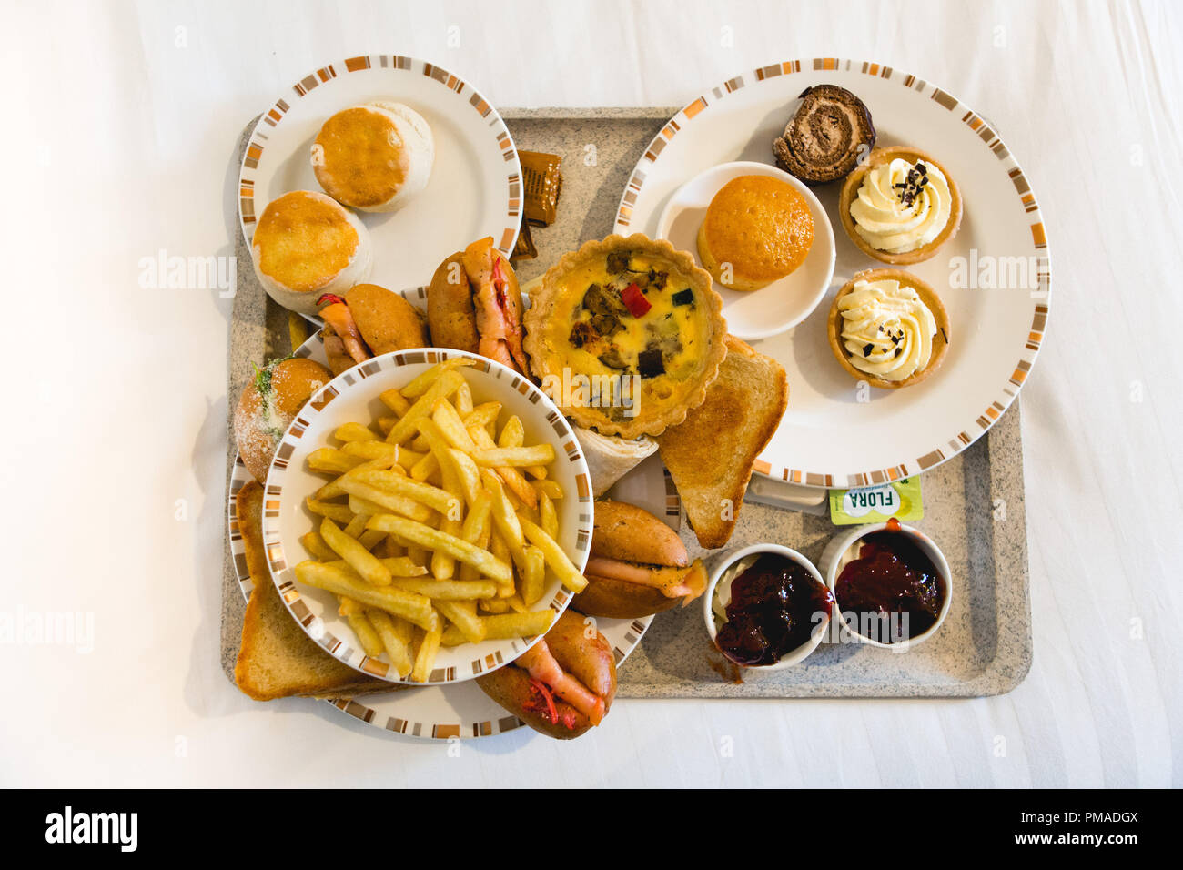 Il vassoio pieno di cibi dolci e salati comprendente le armature di panini, panini, torte, pasticcini, scones & patatine fritte (chip) per il tè del pomeriggio, su un letto Foto Stock