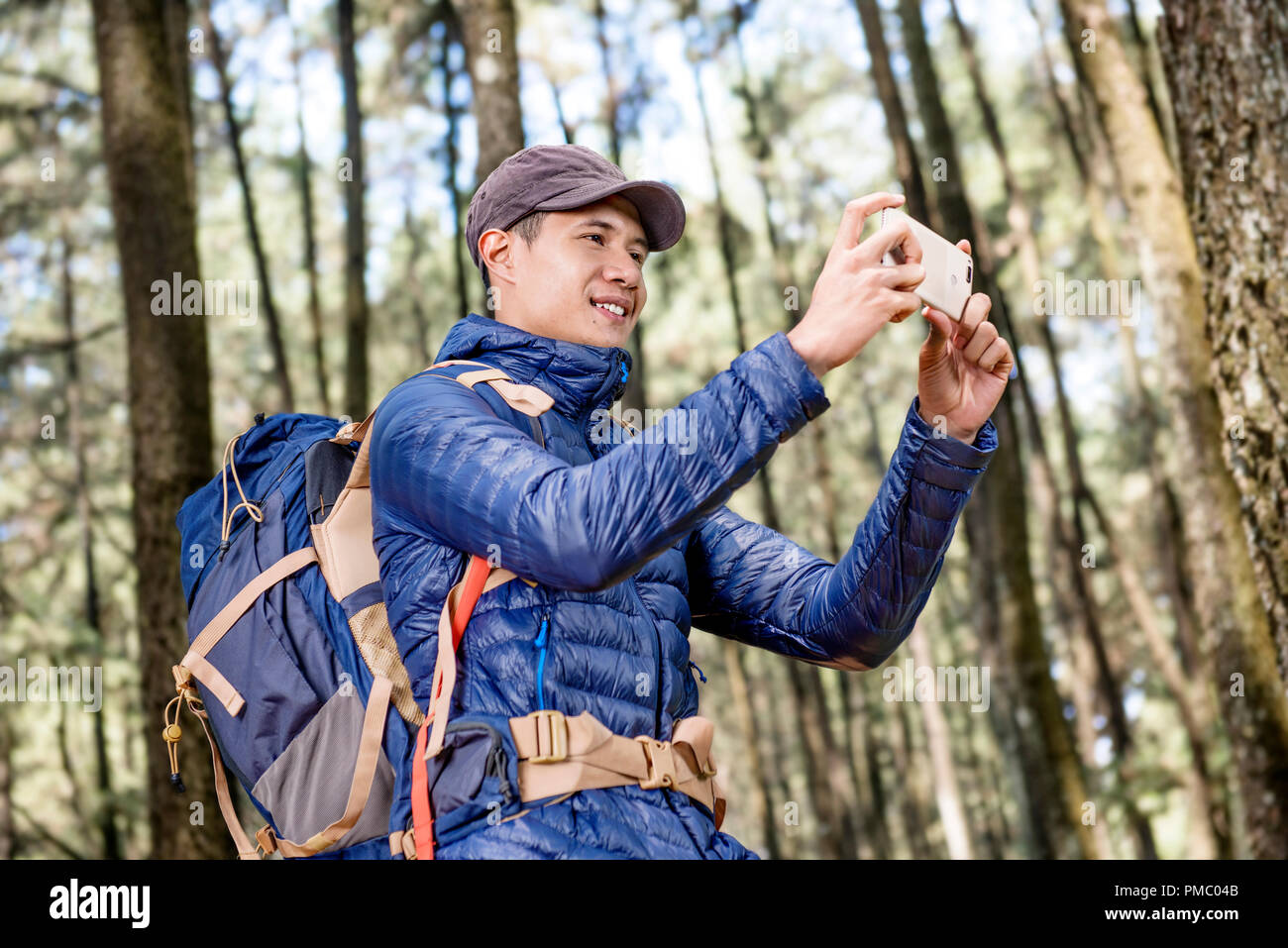 Felice uomo asiatico a scattare foto di foresta con il suo smartphone Foto Stock