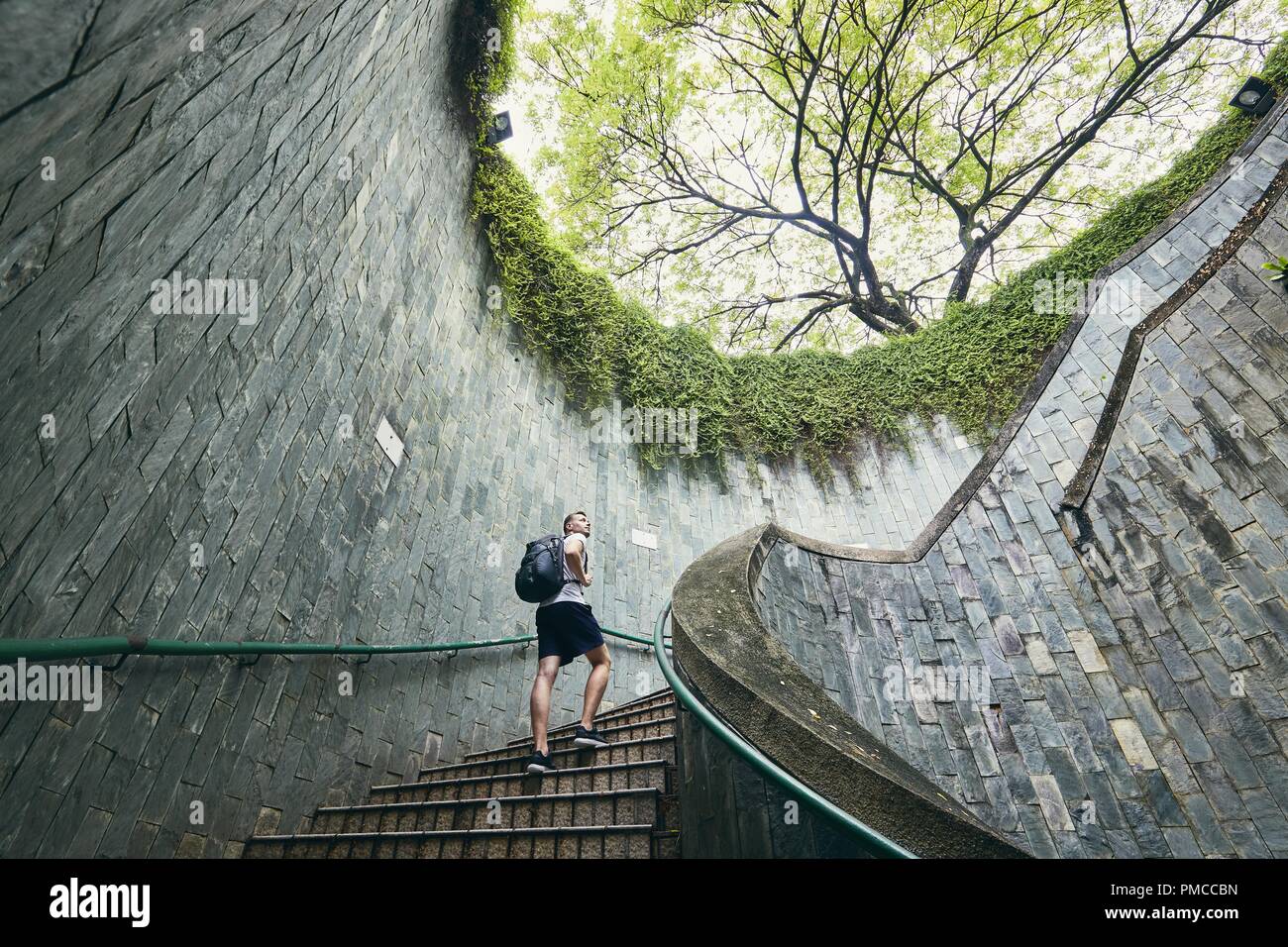 Giovane uomo (turistico) fino a piedi sulla scalinata a spirale di passaggio pedonale sotterraneo in Singapore. Foto Stock