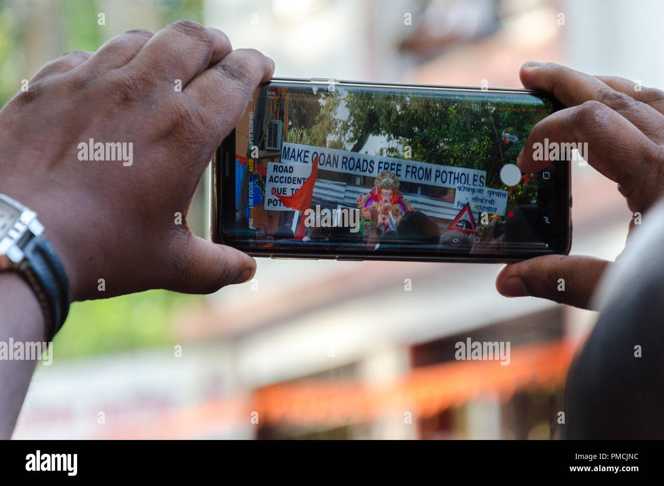 Un telefono cellulare la registrazione di una delle tabelle di immersione con il problema del cattivo stato delle strade di Goan alla cerimonia di immersione in Adpai, Goa. Foto Stock