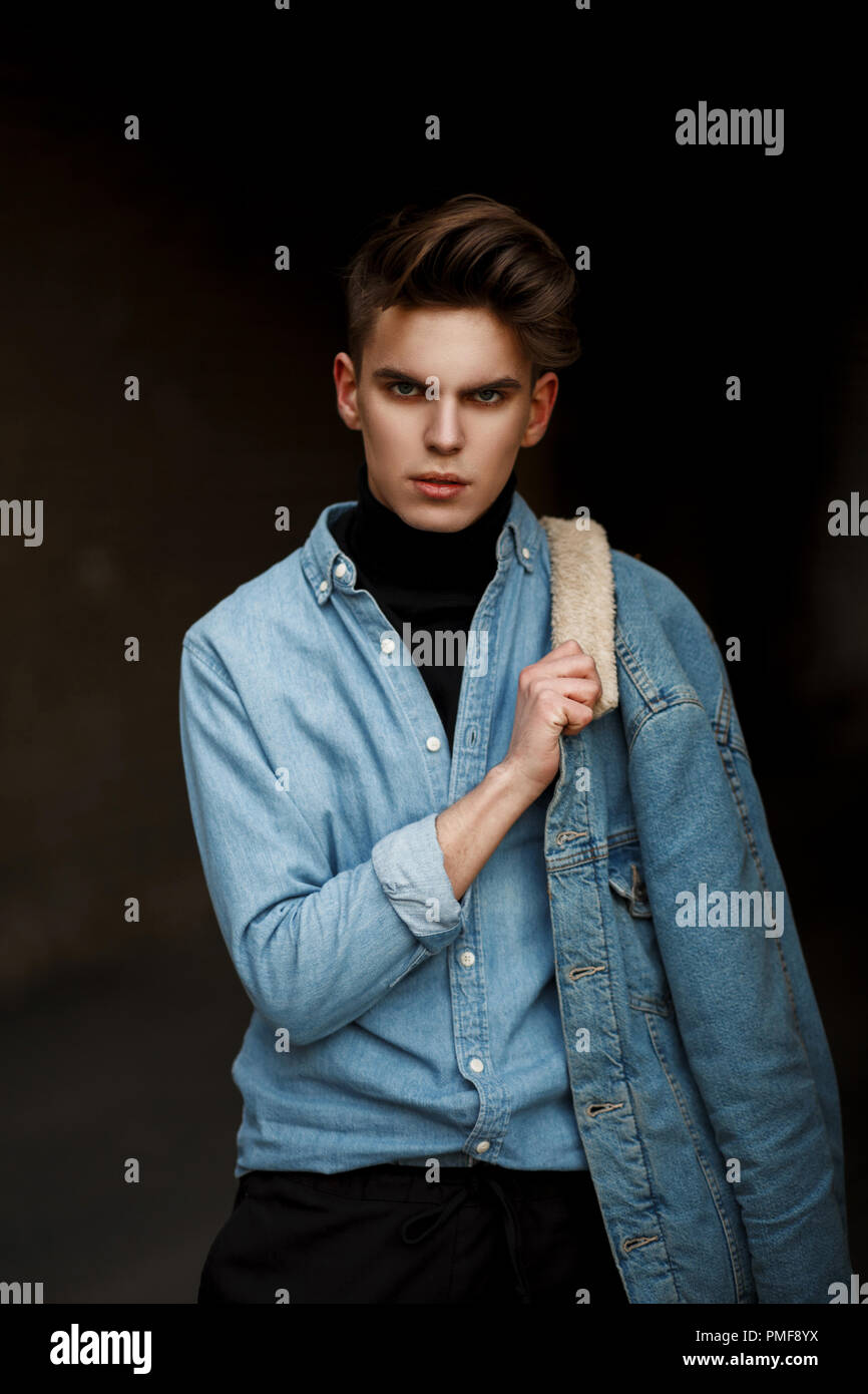 Giovane bello ragazzo con acconciatura in eleganti moda abbigliamento denim  con un paio di jeans in posa sulla strada Foto stock - Alamy