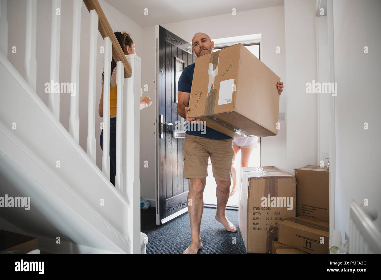 Uomo maturo è portatore di caselle per la sua nuova casa. La figlia e la moglie può essere visto dietro di lui. Foto Stock