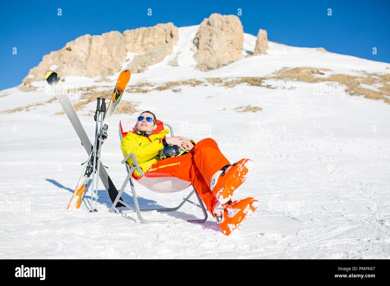 Immagine di sport uomo seduto sulla sedia accanto a sci e bastoni sullo sfondo di montagne innevate durante il giorno Foto Stock