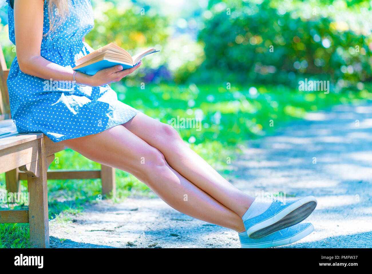 La donna in un vestito blu seduta su una panchina in un parco della città e la lettura di un libro Foto Stock