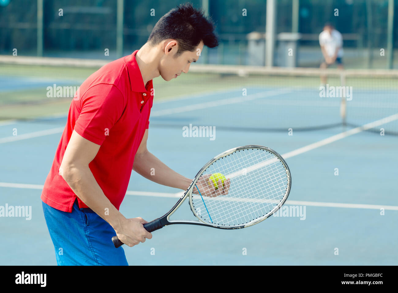 Asian giocatore di tennis guardando la palla con la concentrazione prima di servire Foto Stock