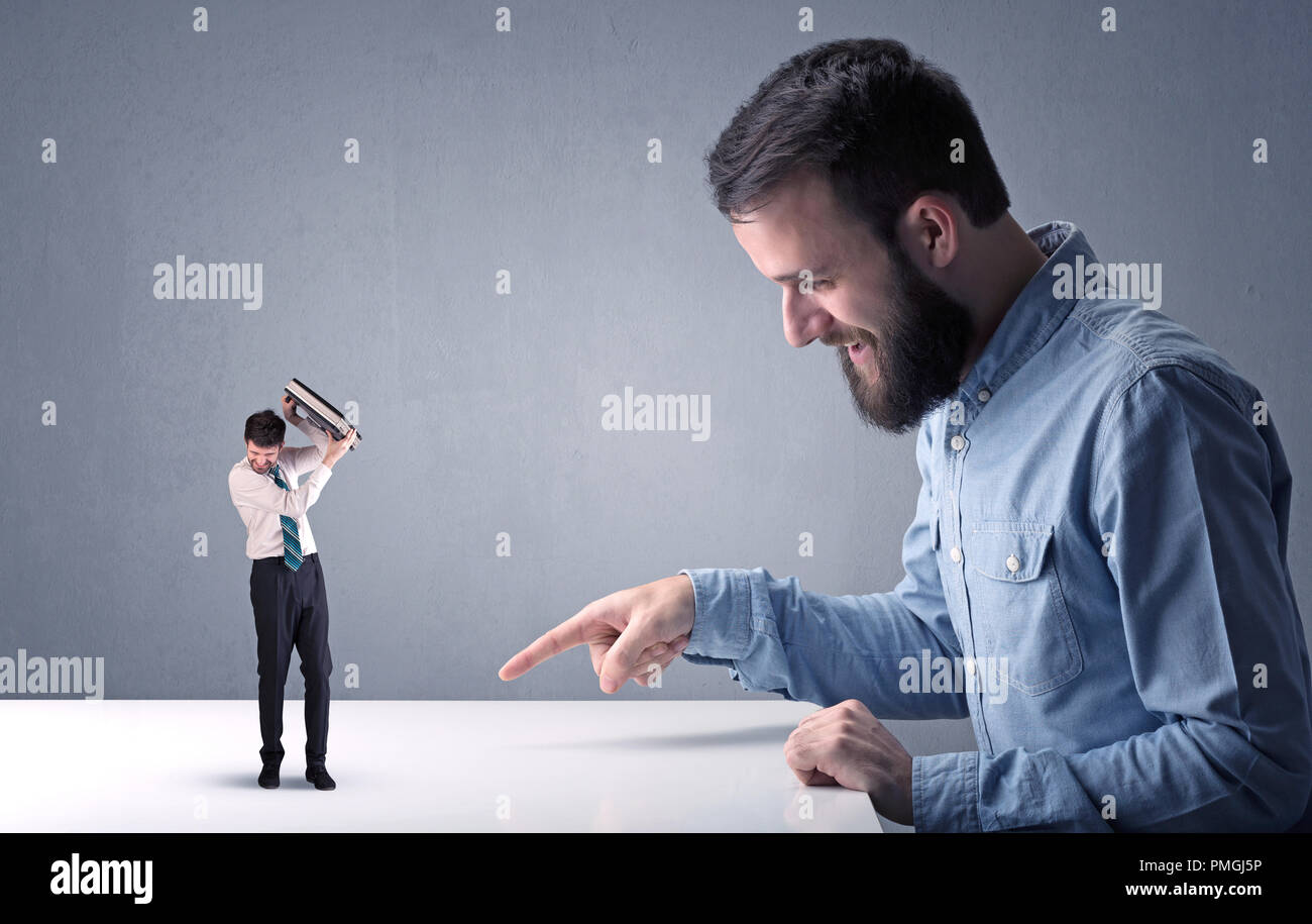 Giovane imprenditore professionale essendo arrabbiato con un altro imprenditore in miniatura nella parte anteriore di un bluastro sfondo grigio Foto Stock