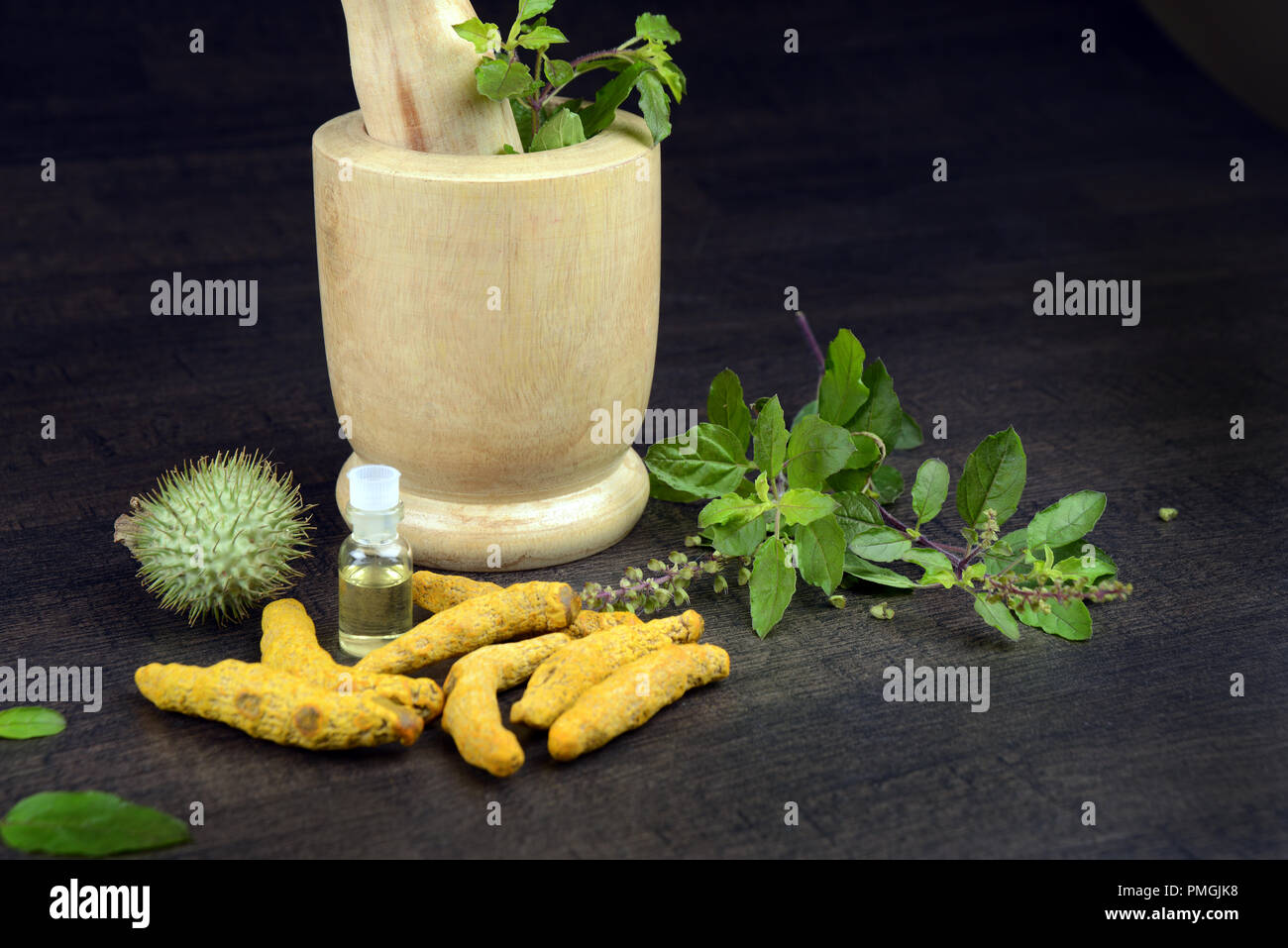 Basilico santo, curcuma, Datura frutta con olio a base di erbe e di mortaio di legno su sfondo scuro, un concetto di Ayurveda Foto Stock