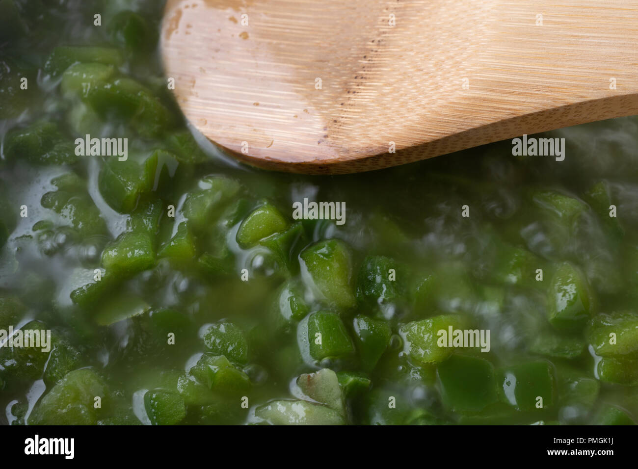 Vista ravvicinata di peperoni verdi tagliati simmering in olio di semi di uva con un cucchiaio di legno. Foto Stock