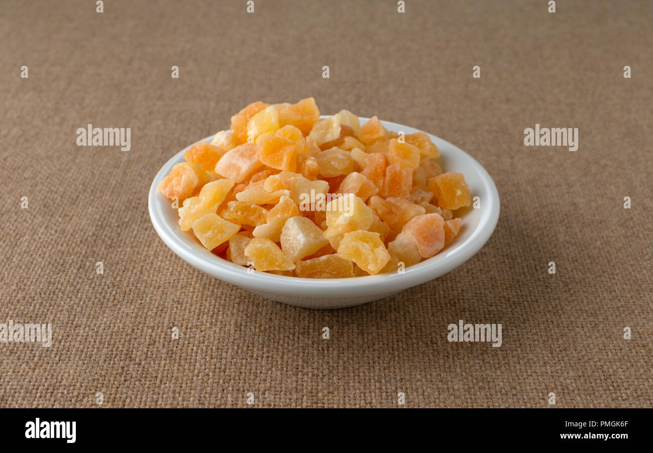 A che serve di essiccati tagliati a dadini di melone in una piccola ciotola bianco su una tovaglia marrone. Foto Stock