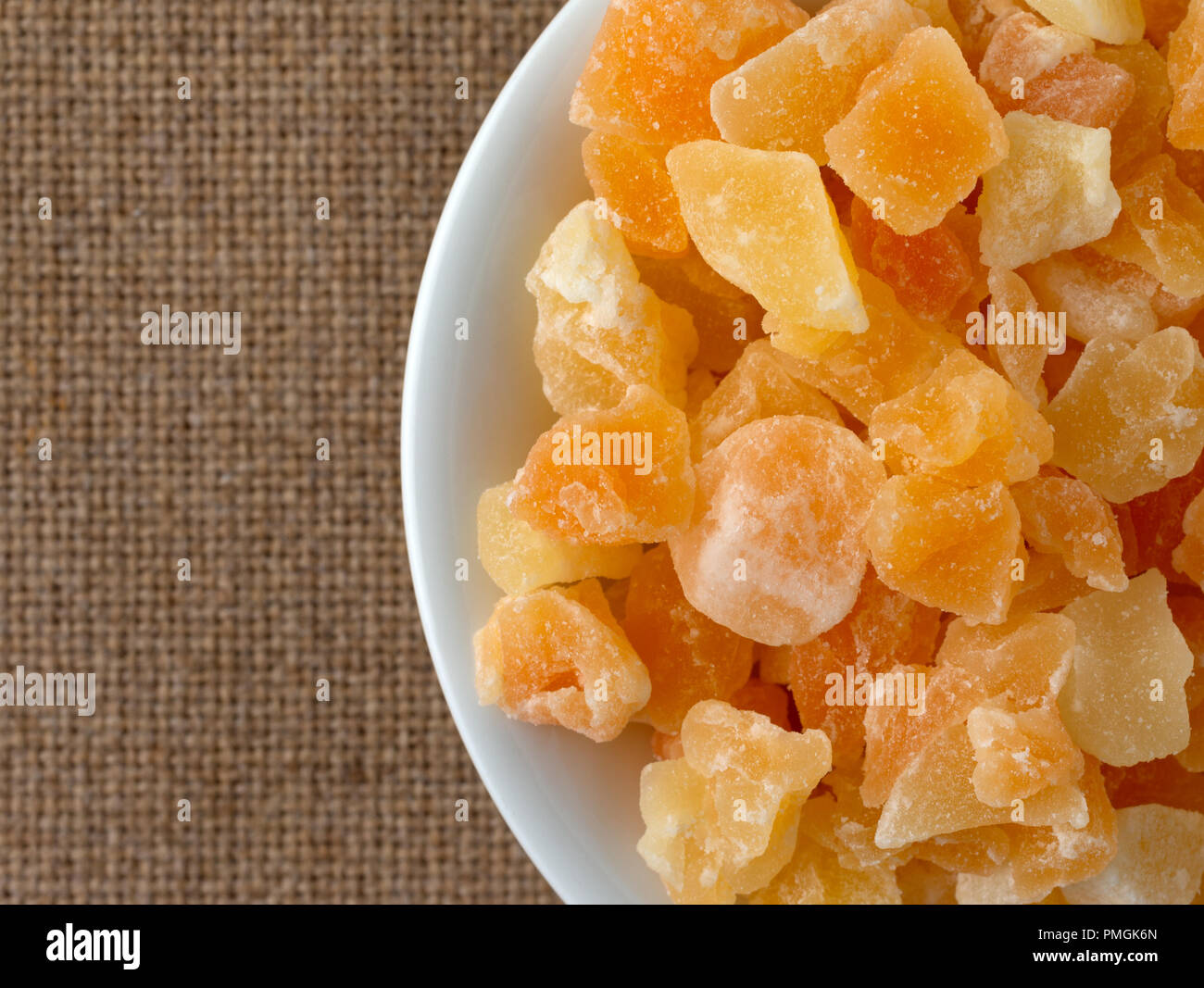Top vista ravvicinata di un serving di essiccati tagliati a dadini di melone in una piccola ciotola bianco su una tovaglia marrone. Foto Stock