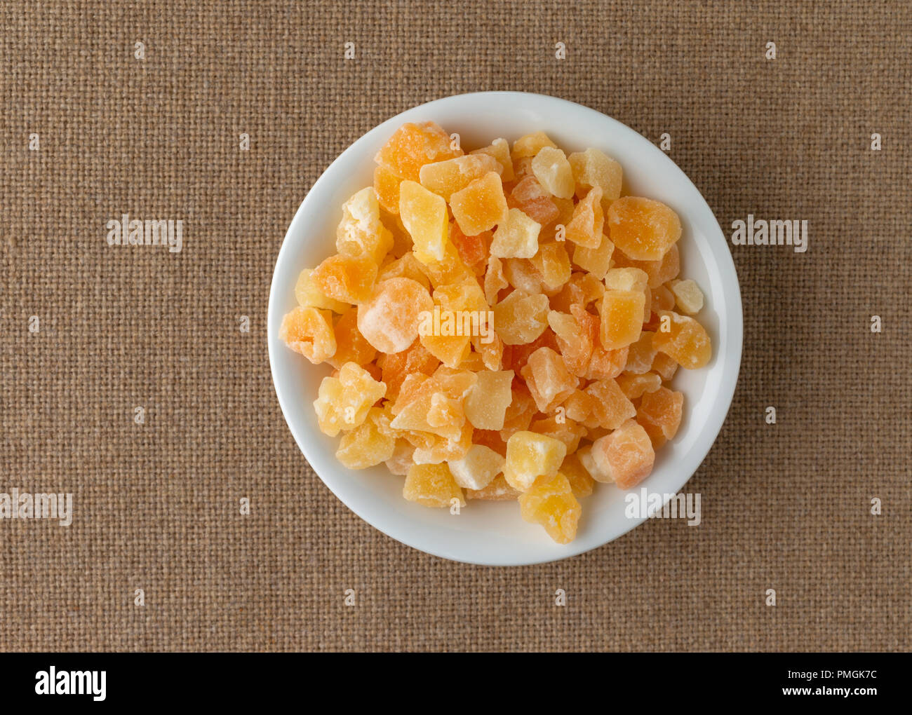 Vista dall'alto di una porzione di essiccati tagliati a dadini di melone in una piccola ciotola bianco su una tovaglia marrone. Foto Stock