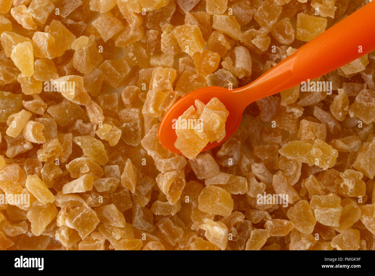 Top vista ravvicinata di zucchero rivestito essiccato a dadini le pesche con un arancione cucchiaio di plastica illuminato con luce della finestra. Foto Stock