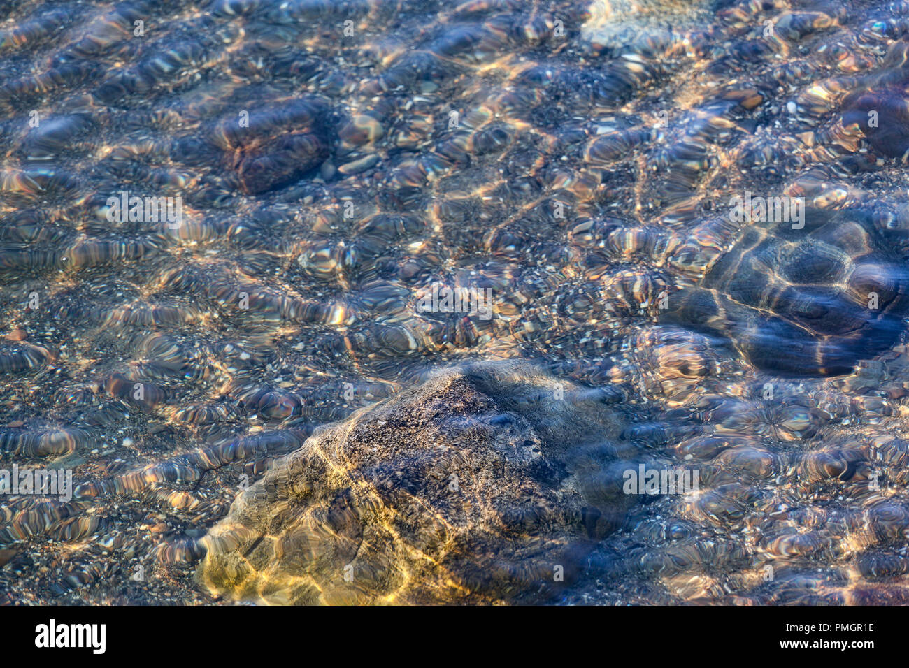 Diversi grandi sassi e ghiaia sul fondo dell'oceano a basso legato con piccole onde luccicante sopra. Foto Stock