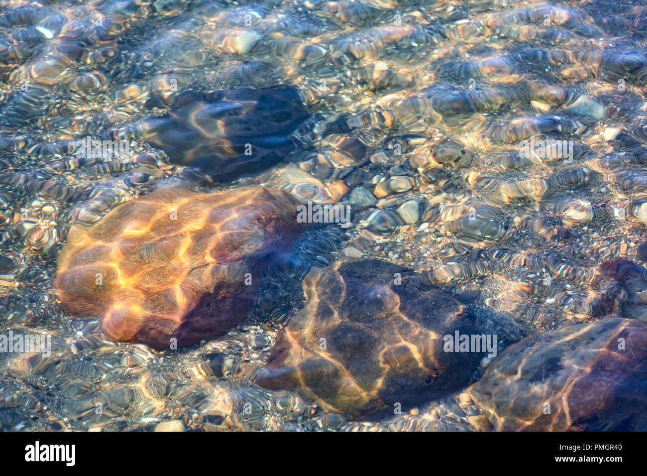 Diversi grandi sassi e ghiaia sul fondo dell'oceano a basso legato con piccole onde luccicante sopra. Foto Stock