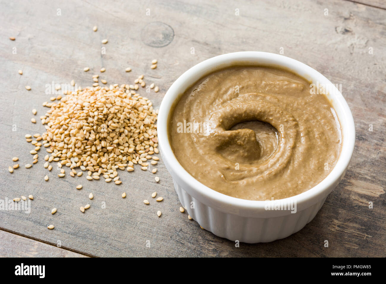 Tahini nella ciotola e semi di sesamo sul tavolo di legno Foto Stock