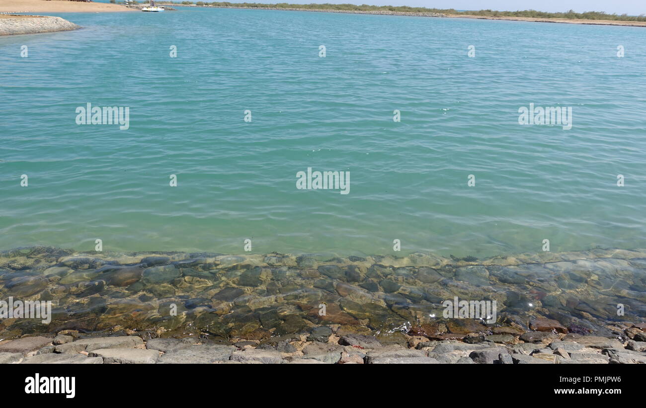 Vista della spiaggia, ampio angolo, paesaggio con mare cristallino, aqua marine, gradiente di profondità di acqua e pietre visibili sul lato mare, baie di corallo Foto Stock